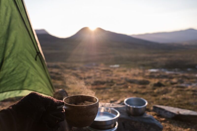 A tranquil camping scene in the Swedish wilderness at sunrise with a steaming cup of coffee.